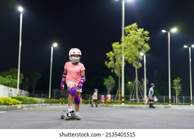 Asian Child Or Kid Girl Playing Surf Skate Or Skateboard In Skating Rink Or Extreme Sports Park At Night To Wearing Face Mask And Helmet With Elbow Pads Wrist And Knee Support For Body Safety Protect