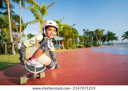 asian child or kid girl playing skateboard or surf skate in skating track and extreme sports exercise by crouching to turn hand touch floor to wearing helmet elbow knee support for body safety protect