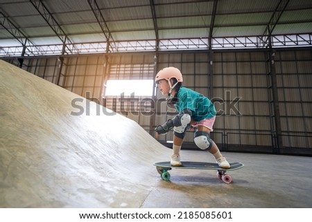 asian child or kid girl playing skateboard or riding surf skate up to wave ramp or wave bank to fun bottom turn in indoor skate park by extreme sports to wearing helmet knee support for body safety