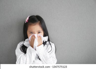 Asian Child Or Kid Girl Sick And Sad With Sneezing On Nose And Cold Cough On Tissue Paper Because Influenza And Weak Or Virus Bacteria From Dust Weather Or Smoke And Kindergarten School For Medical