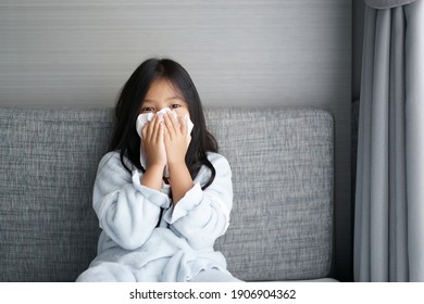 Asian Child Or Kid Girl Sick And Runny Nose Sneezing Or Snot With Cold Cough On Tissue Paper Covering Nose From Influenza Or Coronavirus Covid-19 And Allergy Weak From PM 2.5 Dust At Hospital Or Home