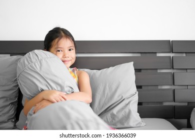 Asian Child Or Kid Girl Sitting Hugging Soft Bolster And Leaning Gray Pillow On Bed Head And Happy Smile To Comfortable Relax On Wake Up Bright After Sleep In Morning And Bedroom At Home For Stay Safe