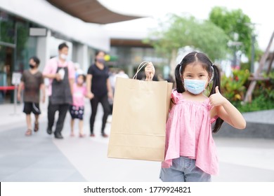 Asian Child Or Kid Girl Smile Wear Face Mask And Holding Empty Recycle Paper Bag To Enjoy Shopping And Fun With Thumb Up For Like And Good At Department Store Or Market Mall To Family Holiday On Covid