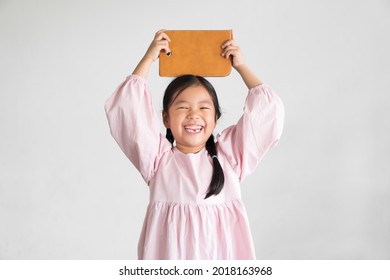 Asian Child Or Kid Girl Smile Laughing Holding And Show Computer Tablet Or Smartphone Pad On Overhead To Learn From Home Or Study Online And Education Communication On White Gray Background Isolated