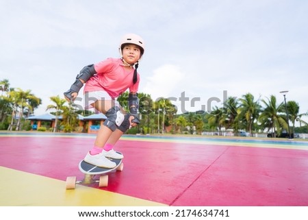 asian child or kid girl smile playing skateboard or surf skate to fun turn in skatepark and extreme sports exercise to wearing helmet elbow pad wrist and knee support for body safety at bang phra park