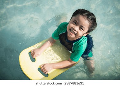 Asian child kid girl smiling funny wearing swimming suit using kick board to swimming or leaning training on swimming pool in water park. Water activity for children on summer holiday. - Powered by Shutterstock