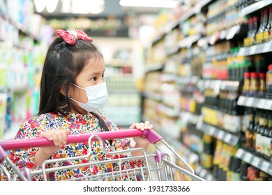 Asian child or kid girl wearing face mask for close mouth nose and flu cough sick to protect coronavirus covid-19 or dust with push supermarket cart for shopping in market mall or department store