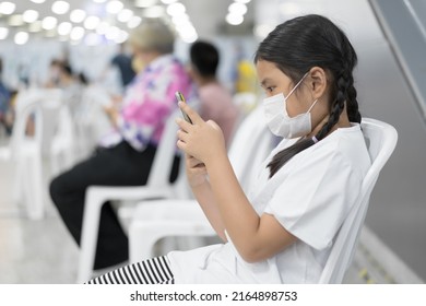 Asian Child Or Kid Girl Wearing White Face Mask Protect Coronavirus And Holding Playing Smartphone To Learning Or Study Online And Communication Or Person Play Mobile Phone On Chair With Lot Of People