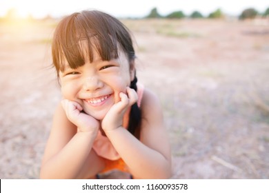 Asian Child Poor Or Kid Girl Smile With Laugh And Happy Fun Because Come Back Home To Country And Wear Traditional Top Or Sleeveless Shirt Sit On Arid Soil For Agriculture At Home And Warm Sunlight