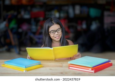 Asian Child Reading Book.Young Female With Books On Table.Student Studying While Sitting Down.Homeschooler Homeschooling.Chinese Girl Learning At Home.Primary Kid Self Study.Happy Person Read.