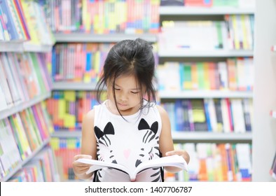 Asian child reading or kid girl happy smile and shopping or choose knowledge or text book on bookshelf in bookstore or library room at kindergarten school or nursery for learn and study with education