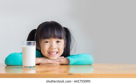 Asian Child Rest Her Chin On Her Hands On The Wooden Table And Smile Behind A Glass Of Milk