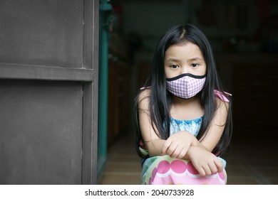 Asian Child Sad Or Kid Girl Wearing Cloth Face Mask For Close Mouth Nose With Cold Cough Sick And Protective Covid-19 Coronavirus Or PM2.5 Dust With Lonely Sit Or Unhappy Absent-minded At Home Door