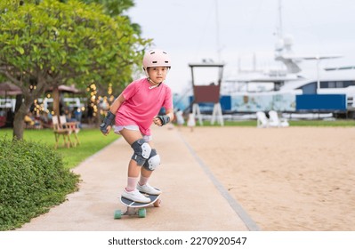 asian child skater or kid girl smile playing skateboard or riding surf skate carving and fun in skate park track on summer beach for extreme sports exercise to wearing helmet wrist guard body safety