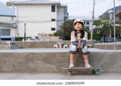 asian child skater or kid girl sitting relax at skatepark with skateboard or surf skate to people extreme sports in skate park by surfskate to wears helmet elbow wrist knee guard for body safety - Powered by Shutterstock