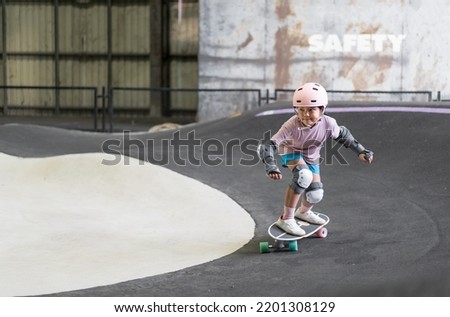 asian child skater or kid girl fun playing skateboard or ride surf skate and turn on pump track in skate park by extreme sports to wearing helmet elbow pads wrist knee support for body safety protect