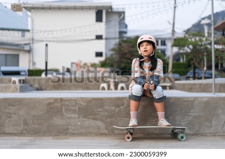 asian child skater or kid girl sitting relax at skatepark with skateboard or surf skate to people extreme sports in skate park by surfskate to wears helmet elbow wrist knee guard for body safety
