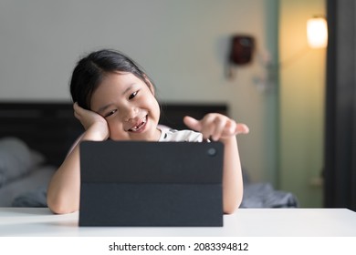 Asian Child Smile Broken Teeth Learning On Computer Tablet Or Kid Girl Student Enjoy To Video Call Studying Or Person Learn From Home School By Study Online Class On Pad In Bedroom With Warm White