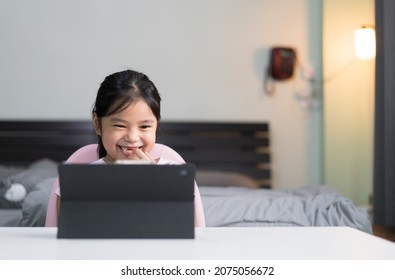 Asian Child Smile Broken Tooth Learning On Computer Tablet Or Kid Girl Student Enjoy To Video Call Studying Or Person Learn From Home School By Study Online Class On Pad In Bedroom With Warm White