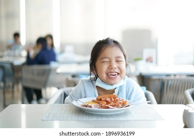 Asian Child Smile Or Kid Girl Wearing Face Mask Under Chin To Enjoy Eating Delicious Food By Sausage Bacon On White Dish With Happy Laugh For Lunch Or Breakfast In Morning At Restaurant Or Food Court