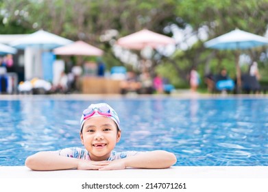 Asian Child Smile Toothless Or Kid Girl Wearing Swimsuit And Cap On Edge Swimming Pool And Happy Fun In Waterpark For Learning Swim To Exercise On Summer School Or Vacation Travel With Copy Space