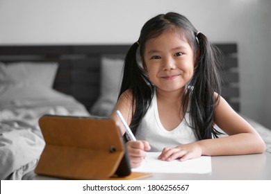 Asian Child Student Back To School Or Kid Girl Smile Write Or Draw And Read On Computer Tablet With Doing Homework To New Idea Think Or People Learn From Home In Bedroom And Study Online On Smartphone