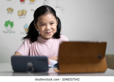 Asian Child Student Learning On Computer Tablet Or Kid Girl Smiling Learn From Home School Or Person Study Online And Video Call On Smartphone With Happy Enjoy To Vocabulary English Words In Classroom