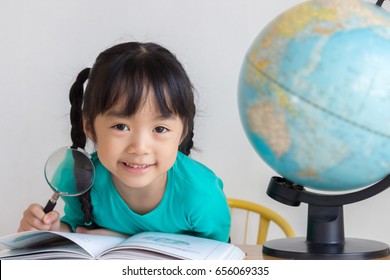 Asian Child Take A Magnifying Glass In Her Hand And Smile And There Are A Book And A Globe Model On The Table