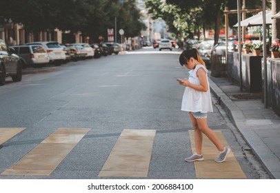 Asian Child Is Watching The Phone On The Road Crossing Or Using A Mobile Phone For A Long Time Hurts Her Eyes And Has An Aggressive Atmosphere. Concept Danger For Children's Mobile Phones.