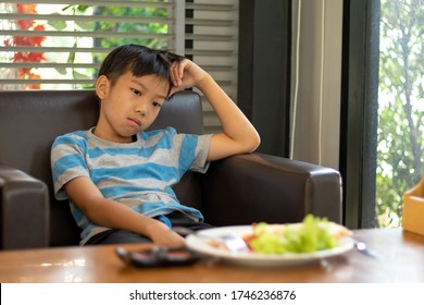 Asian Children Boy Aged 6 To 8 Years Are Sitting With Bored Faces. On The Table In Front Of Him There Was Food. His Face Shows The Dislike Of Food In The Face And Bad Mood.