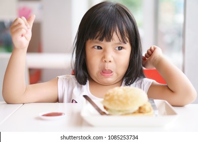 Asian Children Cute Or Kid Girl Eating Ham Burger Or Junk Food With Tomato Sauce On White Dish And Table For Breakfast Or Lunch And Make Face Not Delicious With Unhappy Or Don't Like At Restaurant