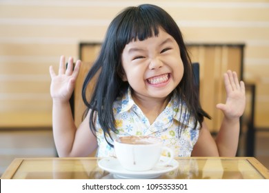 Asian Children Cute Or Kid Girl Smile With Teeth And Delicious Hot Cocoa Or Chocolate Drink In White Cup With Funny And Happy For Breakfast In Morning On Table At Home Or Cafe Restaurant