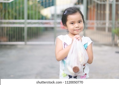 Asian Children Cute Or Kid Girl Smile And Holding Plastic Bag From Shopping Or Buy Food And Snack Or Dessert At Fresh Market For Breakfast Or Lunch On Holiday