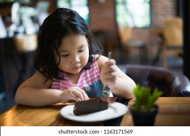 Asian children cute or kid girl enjoy and fun with happy eating delicious brownie chocolate cake for sweet dessert or snack on wood table and make eyeball at lunch in restaurant or cafe