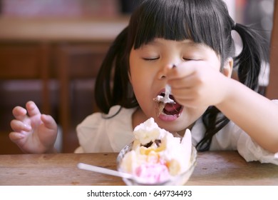 Asian Children Cute Or Kid Girl Enjoy Eating Banana Split Ice Cream With Chocolate For Dessert And Close Eye On The Wood Table And Window Side In The Restaurant