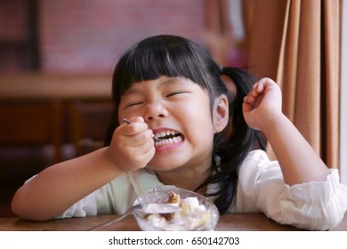 Asian Children Cute Or Kid Girl Enjoy Eating Banana Split Ice Cream And Teeth Smile Or Hypersensitive Teeth On The Wood Table And Window Side With A Curtain In The Restaurant Or Cafe