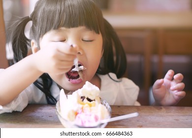 Asian Children Cute Or Kid Girl Enjoy Eating Banana Split Ice Cream With Chocolate For Dessert And Close Eye On The Wood Table And Window Side In The Restaurant With Vintage Style