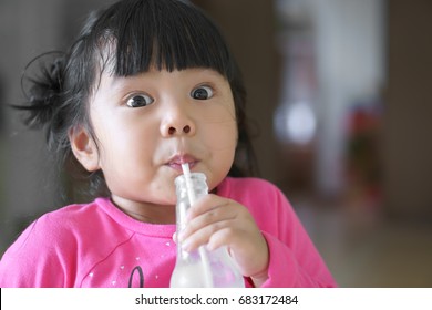 Asian Children Cute Or Kid Girl Drinking Water Or Soy Milk In Bottle By Tube And Make Funny Face With Big Eye For Enjoy And Wearing Pink Shirt With Space