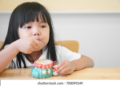 Asian Children Cute Or Kid Girl Happy To Delicious Eating Dessert Or Milk Ice Cream In Colorful Ceramic Cup On The Wood Table In Restaurant Or Cafe For Background With Space