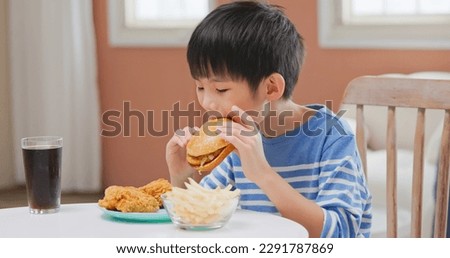 asian children eat unhealthy high calorie sugary junk food such as fried chicken french fries hamburger and coca cola sitting chair by table in the room