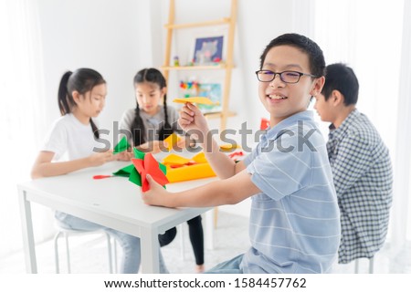 asian children group learning to folding paper in art origami time, asian boy holding his paper plane, they feeling fun and happy, child imagine and development