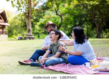 Asian Children And His Grand Parent Picnic In Garden, They Drinking Milk And Eating  Fruit, Retirement Happiness