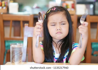 Asian Children Hungry Or Kid Girl Holding Spoon With Fork And Unhappy Or Angry And Touchy Frown For Long Time Wait Eat Delicious Food Or Anorexia And Bored Food For Breakfast In Morning At Restaurant