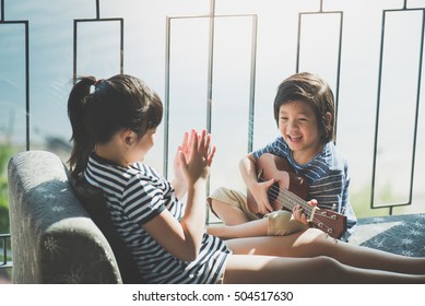 Asian children playing ukulele together near the window