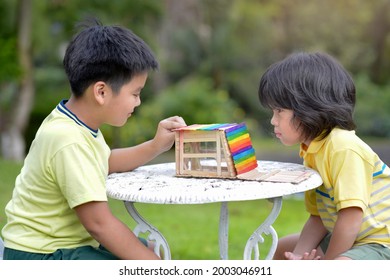 Asian Children With Popsicle Sticks House In The Outdoor.Young Males With Creative Wooden Innovation.Kids Doing Colorful Model Design Craft.Homeschooling Boy Handmade Activity Project.