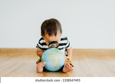 Asian Chinese Baby Boy Looking At Globe Through Magnifying Glass At Home On White Background.Concept For Research Global Warming, Global Network,SEO Search Engine And Kid Education.