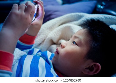 Asian Chinese Boy Playing Smartphone On Bed, Watching Smartphone, Kid Use Phone And Play Game, Child Use Mobile, Addicted Game And Cartoon, 
