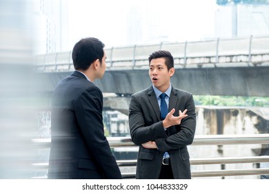 Asian Chinese businessmen standing and talking together outdoors at walkway in the city