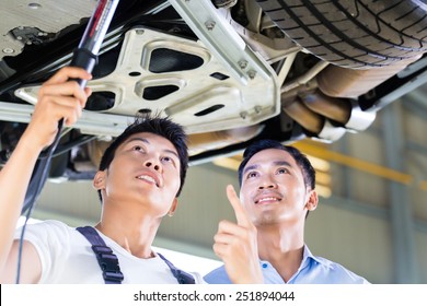 Asian Chinese Car Mechanic With Customer Looking At Auto Floor With Lamp