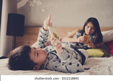 Asian  Chinese Children Playing Tablet With Mother On Bed .  Chinese Child Addicted Phone. Asian Boy Playing Smartphone. Kid Use Telephone. Watching Smartphone

